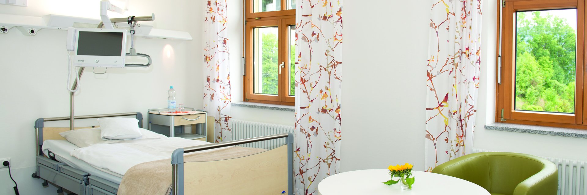 Blick auf ein Zweibettzimmer mit Tisch, Sessel und Bett