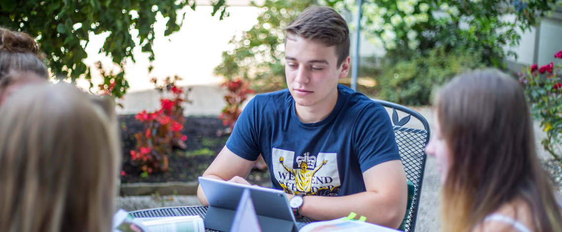 Schüler sitzen draußen an einem Tisch und arbeiten zusammen an Aufgaben