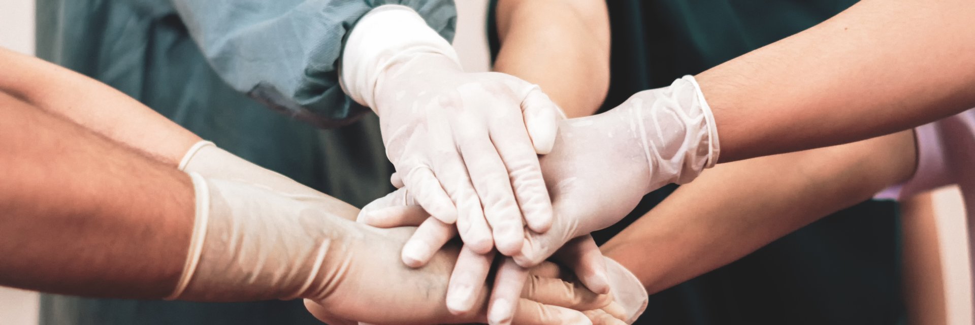 Mehrere Hände mit Handschuhen übereinender, symbolisiert Teamwork