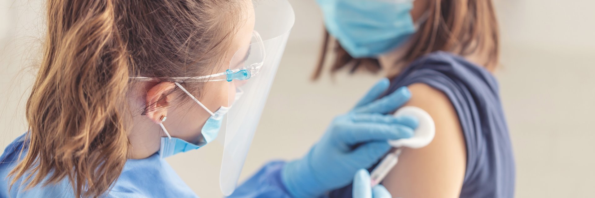 Frau bekommt von einer jungen Angestellten eine Spritze in den Oberarm
