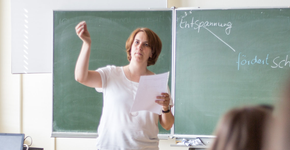 Lehrerin erklärt etwas im Unterricht, Blick auf die Tafel